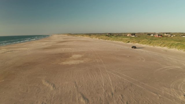 Car driving on a broad beach next to sand dunes and ocean