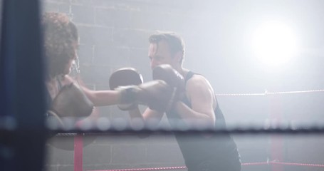 Female boxer with trainer using focus pads