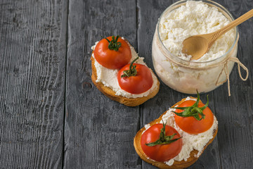 A jar of cottage cheese and bread with cottage cheese and tomatoes on the table.