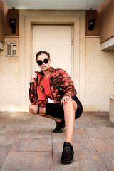 Stylish woman wearing urban style clothes and sunglasses posing near building