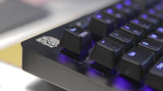Hand pressing a single key on a slightly dusty, black keyboard with blue backlit keys.