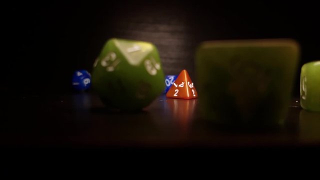 Brown, green and blue polyhedral dice bounce and roll across a table at 240fps, against a black background