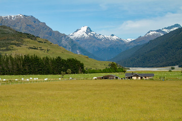 Fototapeta na wymiar Snow capped mountains tower over summer pastures and farm house with a lake in the valley 