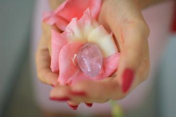 Close up photo of female hand with transparent amethyst yoni egg for vumbuilding inside pink gladiolus flower. Top view of quartz crystal in hands. Womens health concept