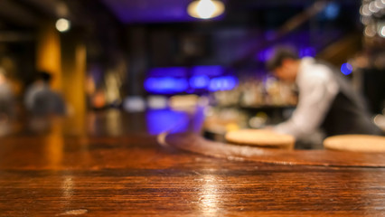 Fototapeta na wymiar Wooden bar table in front of abstract blurred background of restaurant in the dark