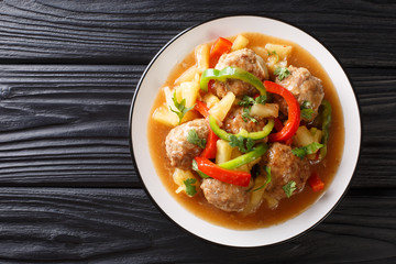 Tasty meatballs with pineapples and vegetables in sweet and sour sauce close-up on a plate. horizontal top view