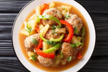 Serving of meatballs with fresh pineapples and bell peppers in sweet and sour sauce close-up on a plate. horizontal top view