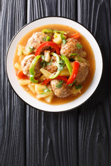 Tasty meatballs with pineapples and vegetables in sweet and sour sauce close-up on a plate. Vertical top view