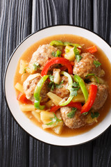 Meatballs cooked with fresh pineapples and vegetables in a sweet and sour sauce closeup on a plate. Vertical top view