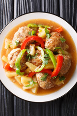 Serving of meatballs with fresh pineapples and bell peppers in sweet and sour sauce close-up on a plate. Vertical top view