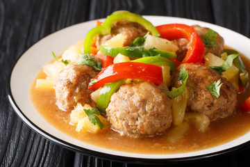 Portion of homemade meatballs with fresh pineapple and bell pepper in sweet and sour sauce close-up on a plate. horizontal