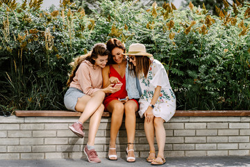 Naklejka premium Beautiful girls using a smart phone and smiling while standing outdoors