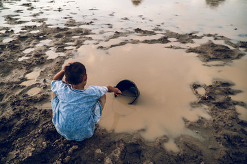 Sad boy scooping water from the lake ,drought and global warming.