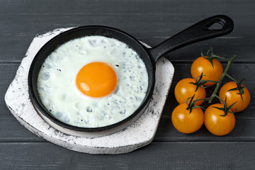 fried eggs in cast iron pan on white wooden stand with yellow cherry tomatoes. Easy healthy breakfast.