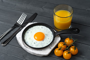 fried eggs in cast iron frying pan on white wooden stand with yellow cherry tomatoes and orange juice. Easy healthy breakfast.