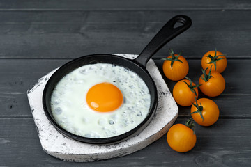 fried eggs in cast iron pan on white wooden stand with yellow cherry tomatoes. Easy healthy breakfast.