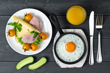 Breakfast of fried eggs in pan, toast with cheese, ham, lettuce, cherry tomatoes, cucumbers and orange juice. Delicious nutritious breakfast.
