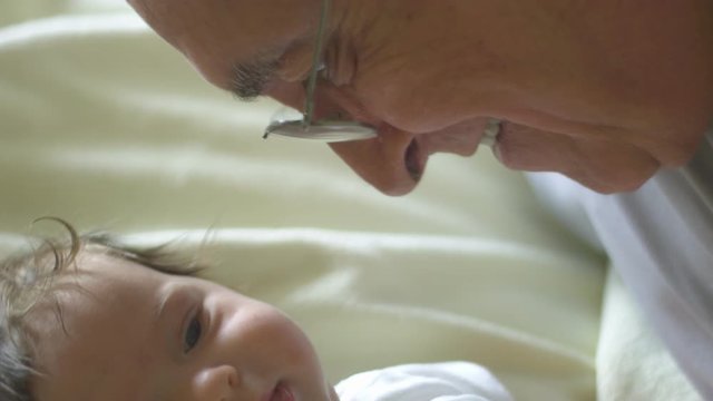 Slow motion of baby smiling at camera as grandfather talks to her
