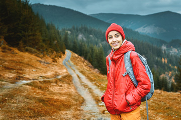 woman hiker with backpack, wearing in red jacket and orange pants, standing on the mountains and...