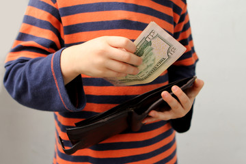 child, preschooler, primary school student, takes out money, dollars, euros from a leather wallet,...