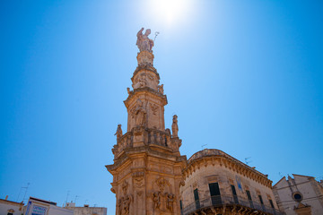 Close up of details of baroque obelisk of Sant'Oronzo in Ostuni filled with light, Puglia, Italy. Clean blue sky. Baroque monument in the White city Ostuni.