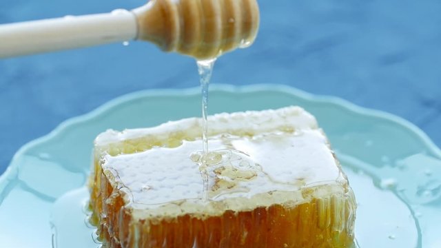 Natural Eco Food Concept. Hand holds spindle for honey. Sweet honeycombs in a plate