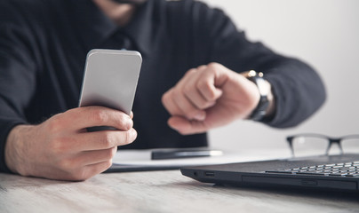 Businessman using smartphone and looking at wristwatch.
