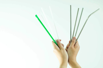 Hands hold plastic straws vs stainless straws on white background.