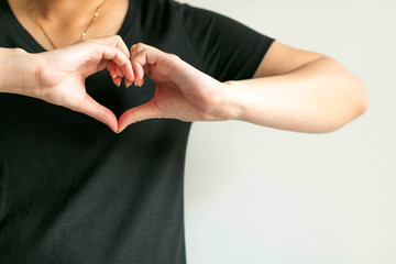 A woman use hands display love symbol by splice fingertips together to be heart shape place at front of left chest.