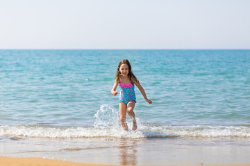 Fototapeta na wymiar little happy girl in bright swimsuits play on the beach. Children on vacation. Family vacation