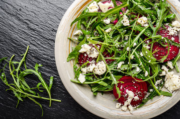 Top view at clay dish with beetroot arugula and feta cheese salad on slate stone tray closeup view