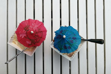 Ice cream in a bowls with spoons and sun umbrellas decoration on the wooden table top view