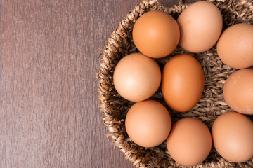 Top view of organic raw chicken eggs in bamboo basket with copy space on brown wooden floor background