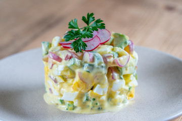 Delicious salad with cucumber, radish and egg with cream sauce in a plate on wooden background. Healthy food, close up