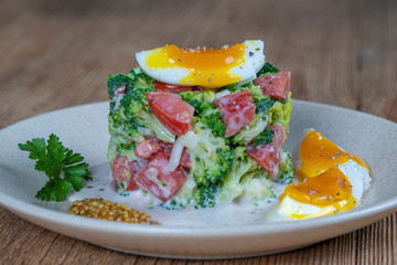 Delicious salad with broccoli, tomato, onion and boiled egg with cream sauce in plate on wooden background. Healthy food