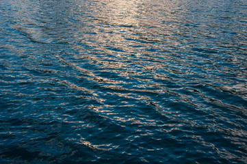 glare on the surface of the water in the sea and the waves behind the sunset.