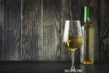 Transparent bottle of white dry wine on the table. White wine glass on a wooden background.