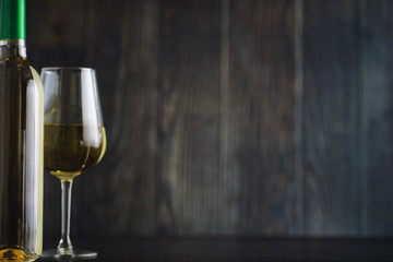 Transparent bottle of white dry wine on the table. White wine glass on a wooden background.