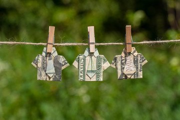 Origami shirt made of dollar banknote on hanging green nature background. Dollar bills hanging on a rope. Close up