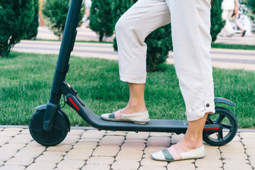 Obraz premium Woman riding an electric scooter in park, view of legs.