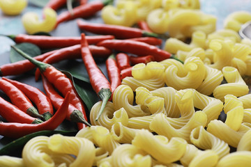 Uncooked pasta on a stone background. With seasonings and spices, spicy chili peppers.