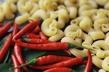 Uncooked pasta on a stone background. With seasonings and spices, spicy chili peppers.
