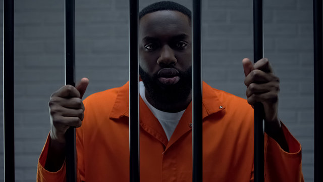 Black prisoner holding bars and looking at camera, drug dealer punishment