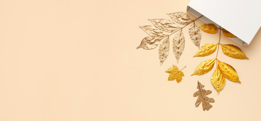 Flat lay creative autumn composition. White Gift Paper package and Golden leaves on beige background top view copy space. Fall concept. Autumn background. Minimal concept idea, floral design