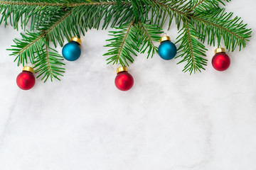 Fir-tree branches decorated with red and blue balls on gray marble background. New Year, Christmas and winter concept. Flat lay, top view, free copy space.