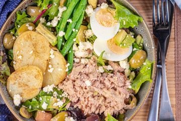 A traditional French 'Nicoise Salad' with a blue napkin on a bamboo placemat
