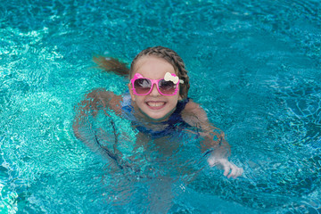 Naklejka premium Portrait of cute happy little girl having fun in swimming pool. Kids sport on family summer vacation. Active healthy holiday