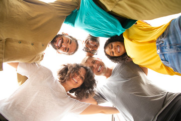 Group portrait of happy close friends hugging outside. Bottom view of young men and women standing in circle and embracing each other. Friendship and unity concept