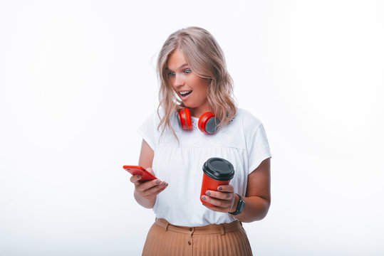 Photo of young woman, looking shocked at moile while holding a cup of coffee, isolated background