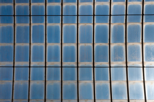 Blue glass roof ceiling with abstract square shape pattern seen from under below against clear sky.